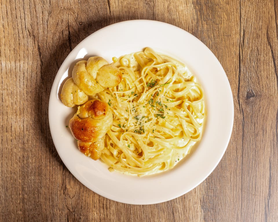 Creamy fettuccine alfredo with grated cheese and parsley, served with two garlic knots on a white plate.