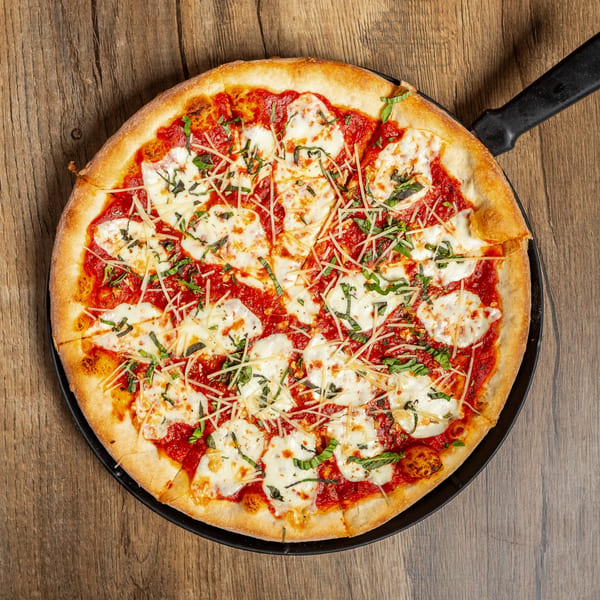 A whole Margherita pizza with fresh basil, mozzarella, and tomato sauce in a black pan.