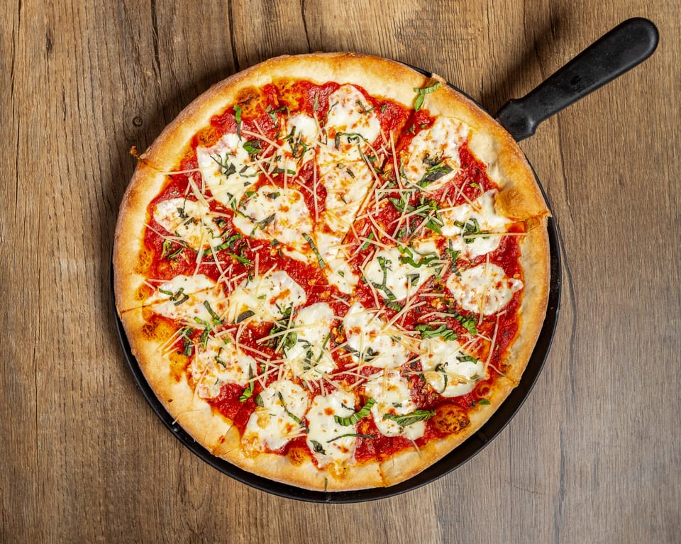 A whole Margherita pizza with fresh basil, mozzarella, and tomato sauce in a black pan.