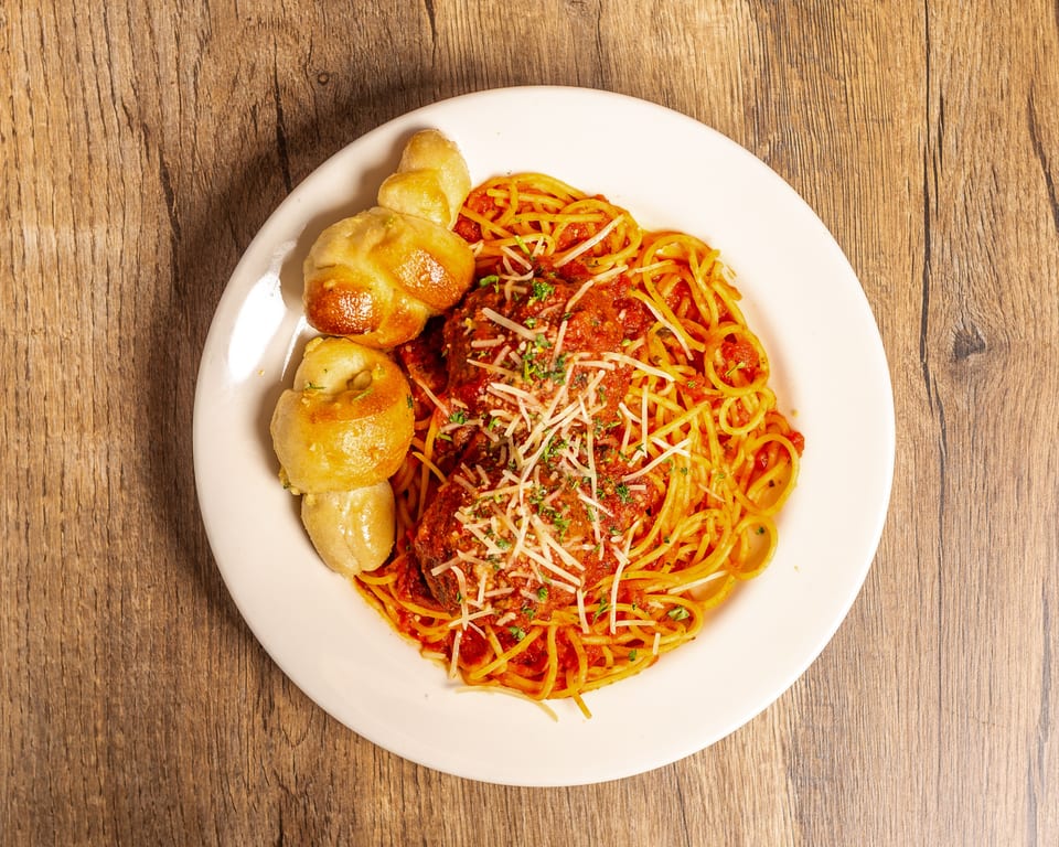 Spaghetti with meatballs and tomato sauce, topped with parmesan cheese and parsley, served with garlic knots.