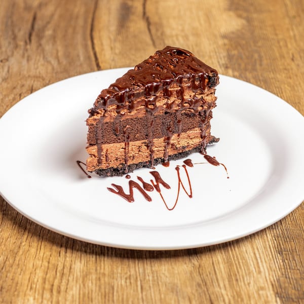 A slice of chocolate cake with multiple layers of frosting and chocolate drizzle on a white plate.