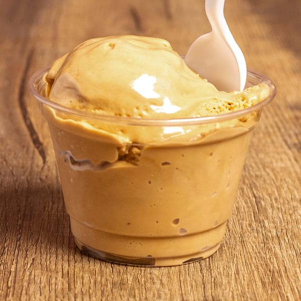 A clear cup of creamy caramel ice cream with a white spoon on a wooden table.
