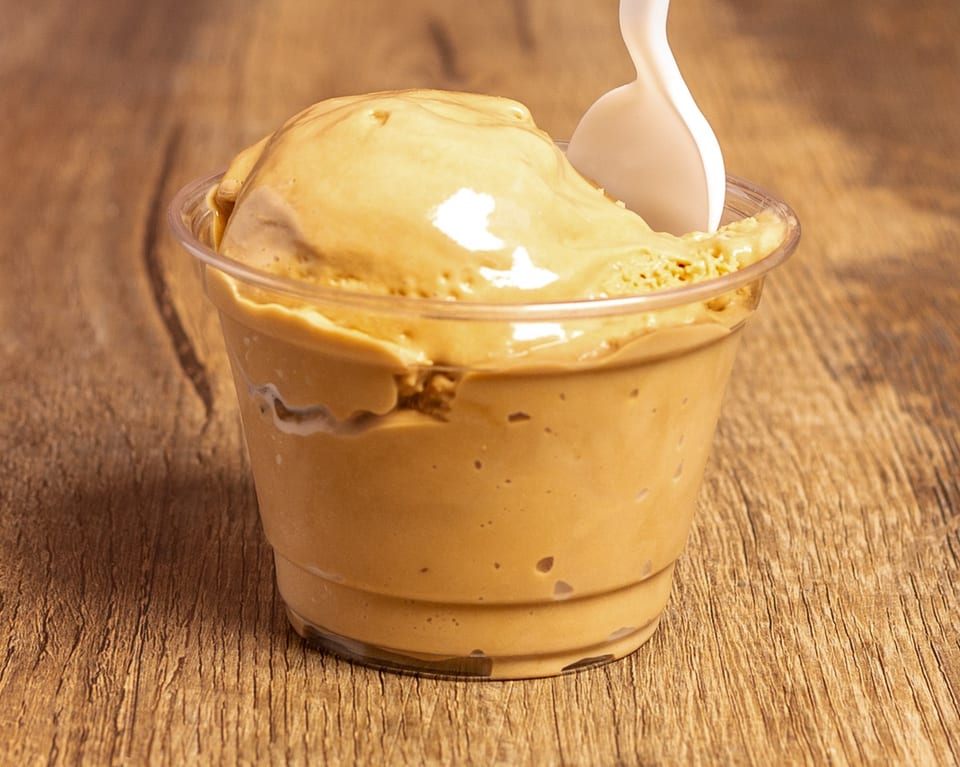 A clear cup of creamy caramel ice cream with a white spoon on a wooden table.