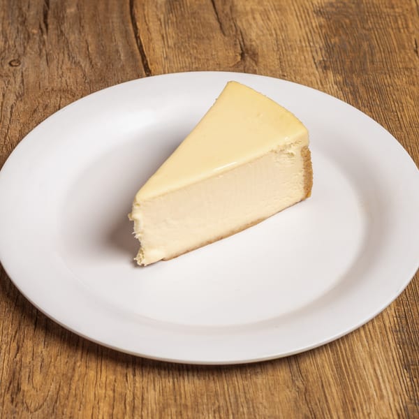 A single slice of plain cheesecake with a graham cracker crust on a white plate.