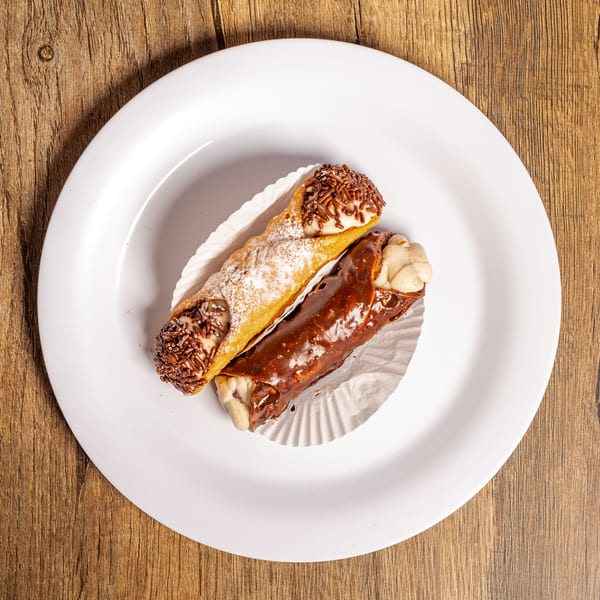 Two cannolis, one with chocolate sprinkles and one with chocolate glaze, on a white plate.