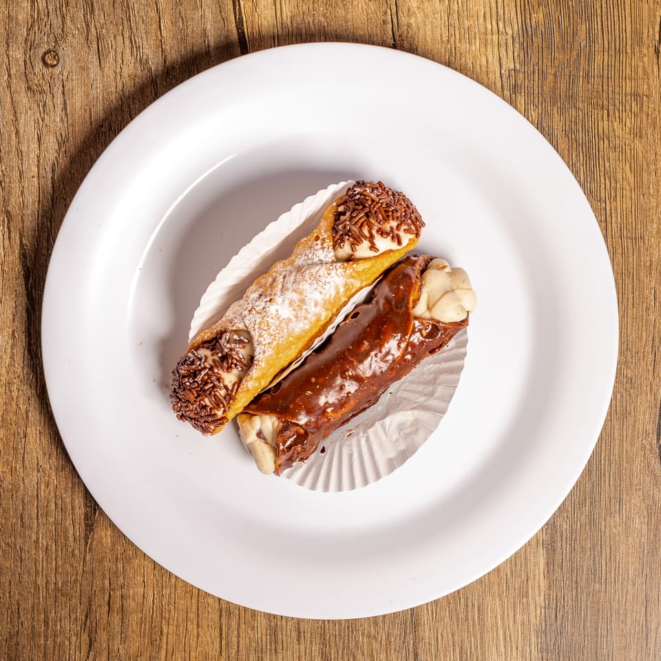 Two cannolis, one with chocolate sprinkles and one with chocolate glaze, on a white plate.