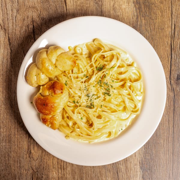 Creamy fettuccine alfredo with grated cheese and parsley, served with two garlic knots on a white plate.