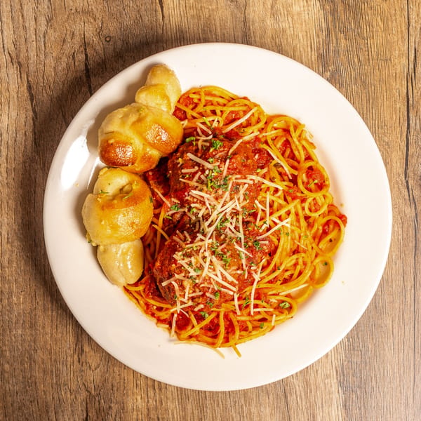 Spaghetti and meatballs with marinara sauce, parmesan cheese, and garlic knots on a white plate.