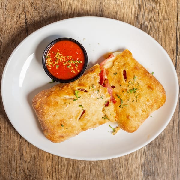 Golden-brown calzone with melted cheese and pepperoni, served with a side of marinara sauce.