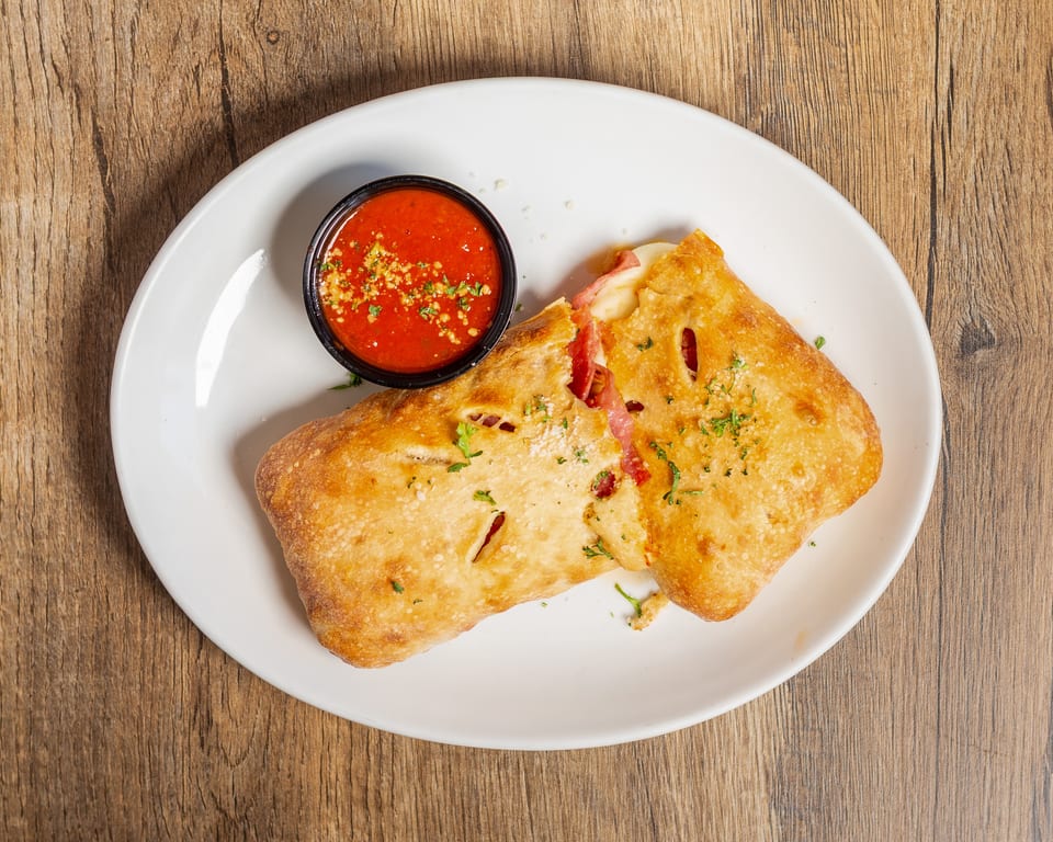 Golden-brown calzone with melted cheese and pepperoni, served with a side of marinara sauce.
