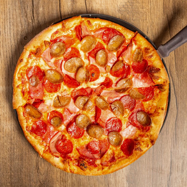 Overhead view of a whole pepperoni, ham, and sausage pizza on a dark pan.