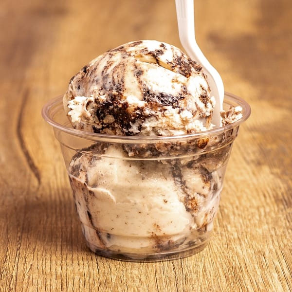 Two scoops of cookies and cream ice cream in a clear cup with a white spoon.