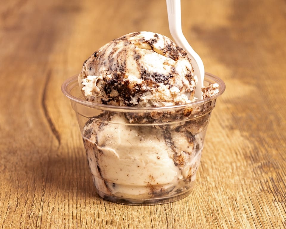 Two scoops of cookies and cream ice cream in a clear cup with a white spoon.