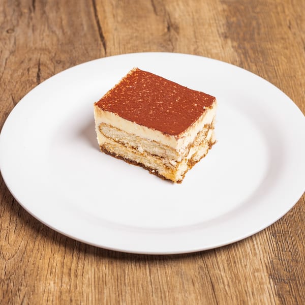 A rectangular slice of tiramisu with cocoa powder on top, served on a white plate.