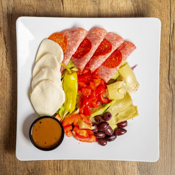 Antipasto salad with salami, pepperoni, mozzarella, peppers, olives, artichokes, and dressing on a white plate.