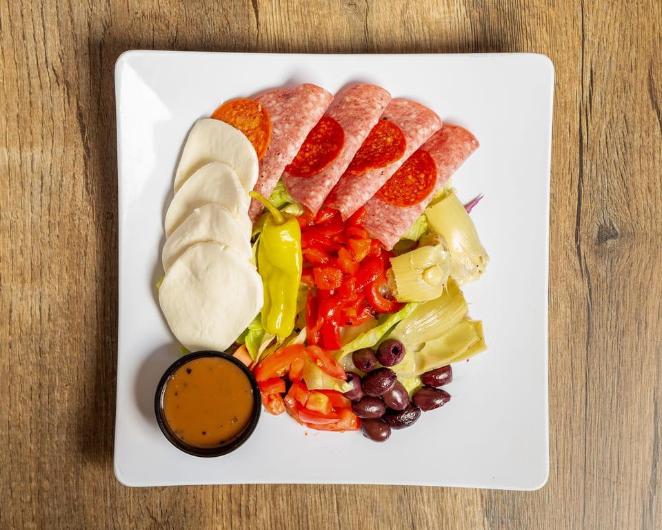 Antipasto salad with salami, pepperoni, mozzarella, peppers, olives, artichokes, and dressing on a white plate.