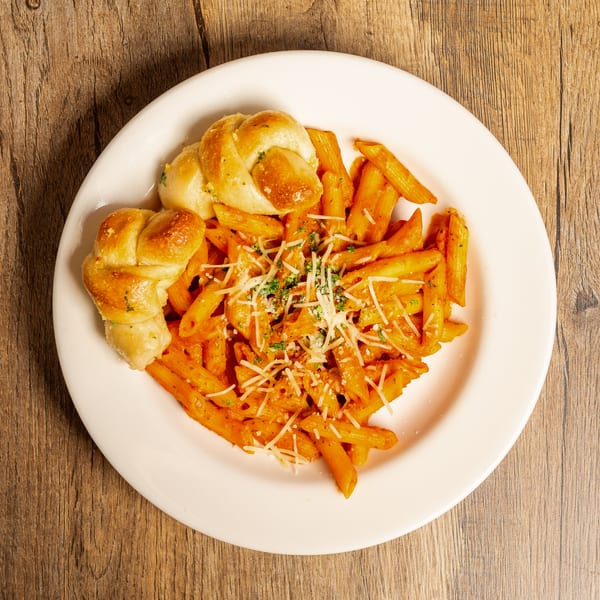 Penne pasta in red sauce with grated cheese and two garlic knots on a white plate.