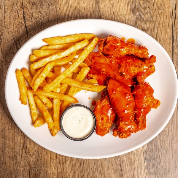 A white oval plate with buffalo wings, french fries, and a side of ranch dressing.