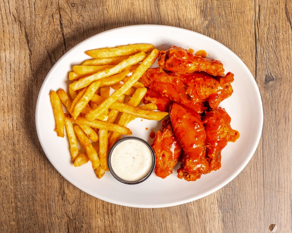 A white oval plate with buffalo wings, french fries, and a side of ranch dressing.