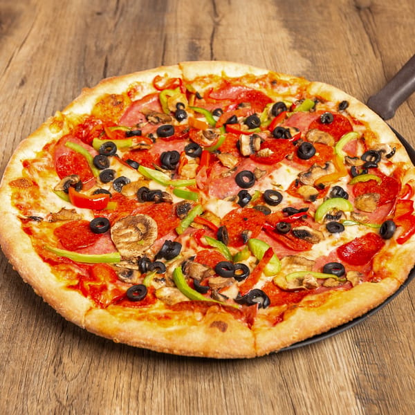 A whole pizza with pepperoni, olives, mushrooms, and bell peppers on a wooden table.