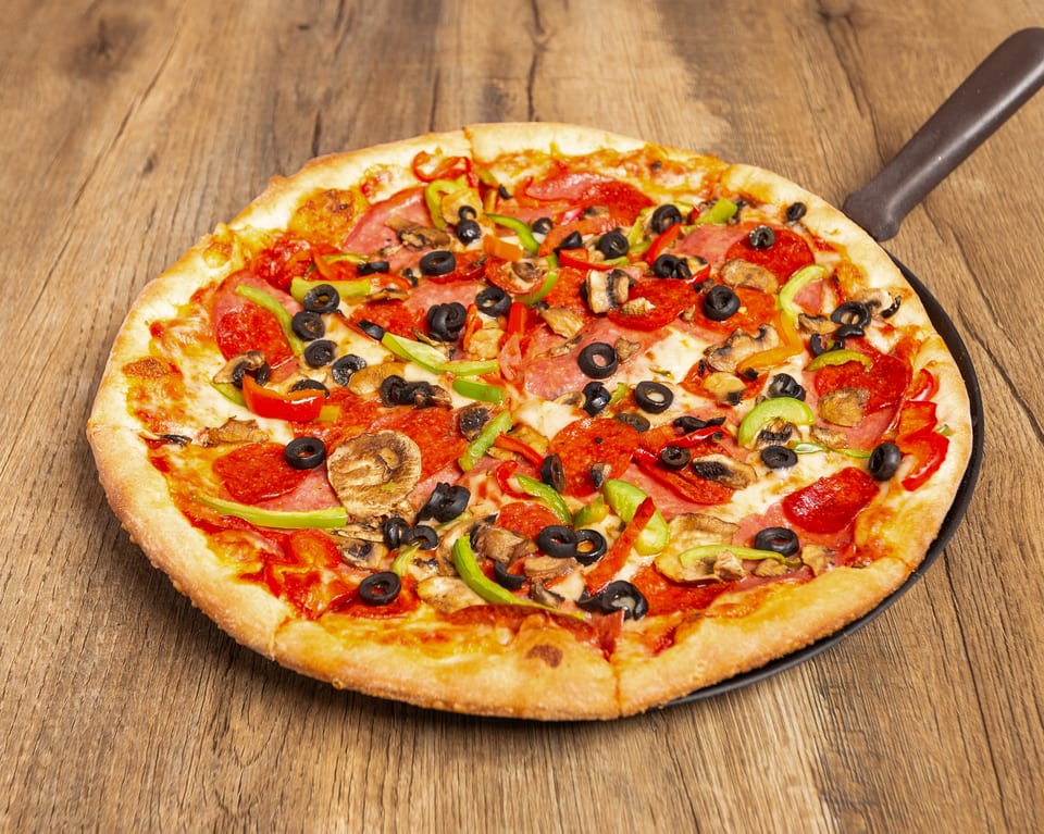 A whole pizza with pepperoni, olives, mushrooms, and bell peppers on a wooden table.